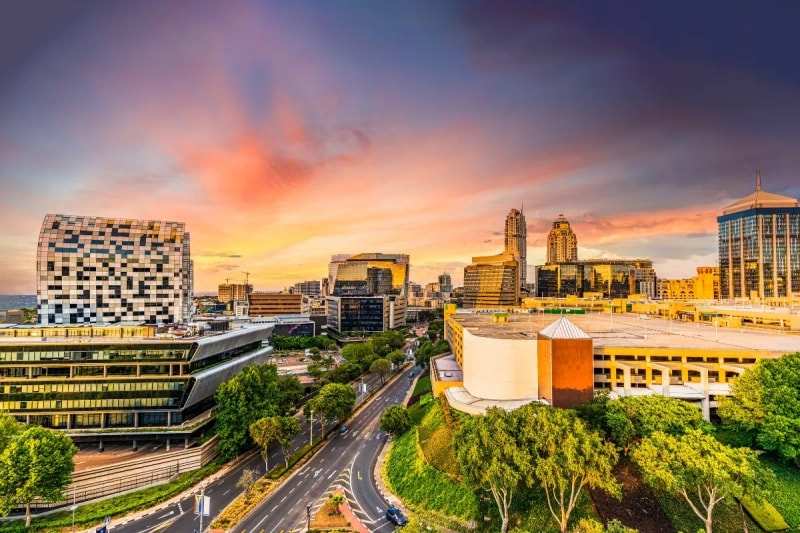 Office towers and a curving road in Johannesburg under a red and violet sunset sky