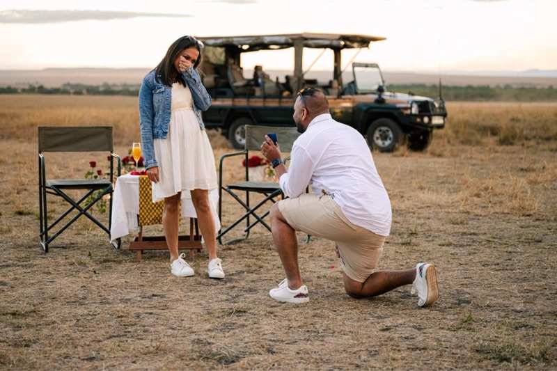 A marriage proposal on one knee beside a safari vehicle in the bush