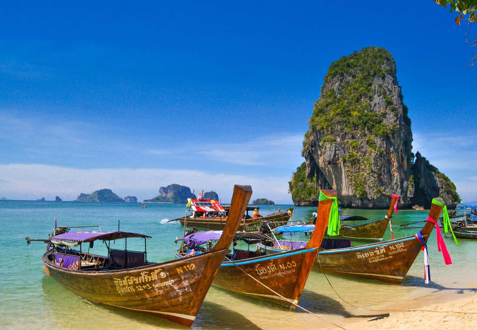 Long-tail boats moored on the sand below a limestone stack on Thailand's Andaman coast