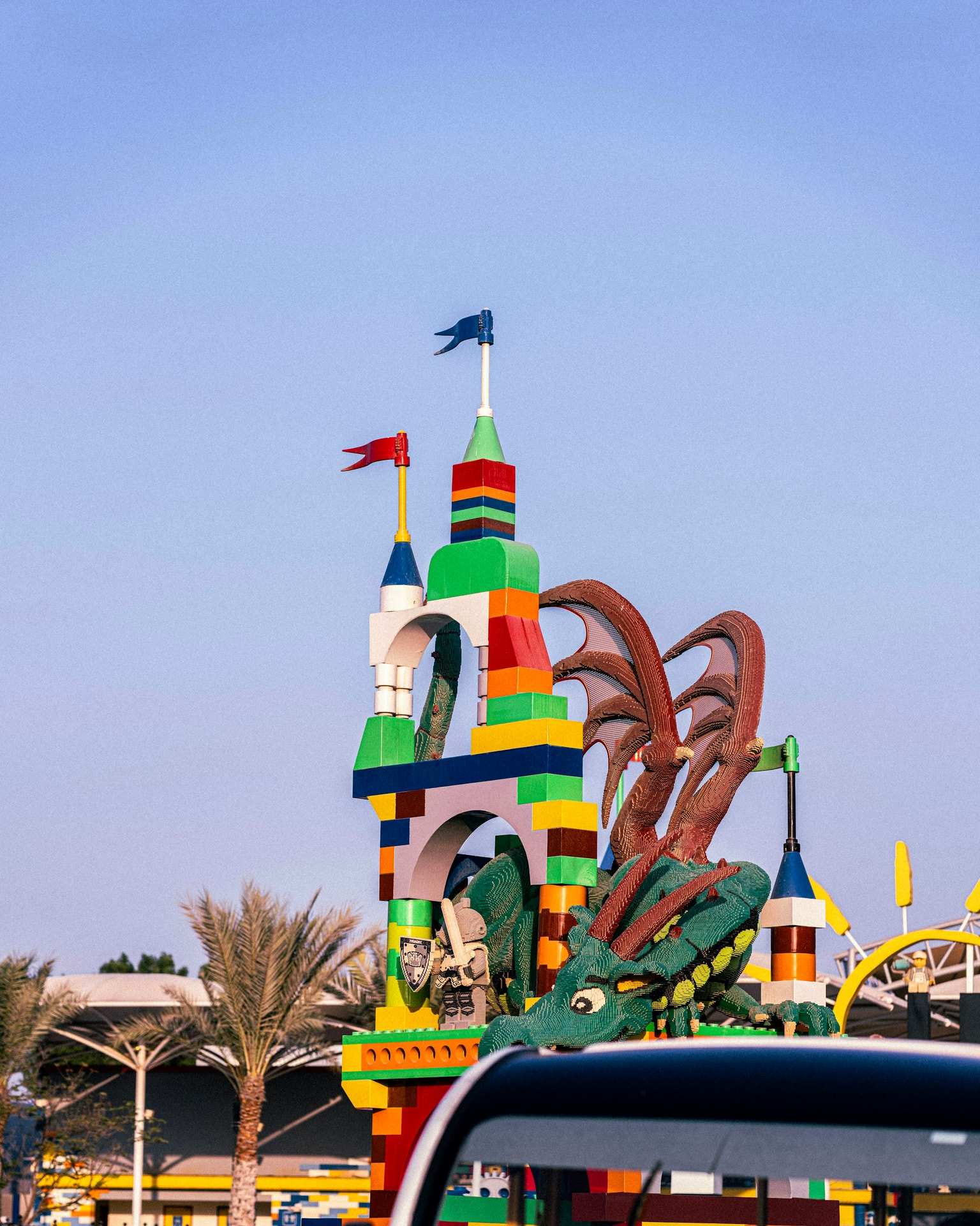 A tower and a dragon built from giant Lego bricks under a blue sky in Dubai, flags on top