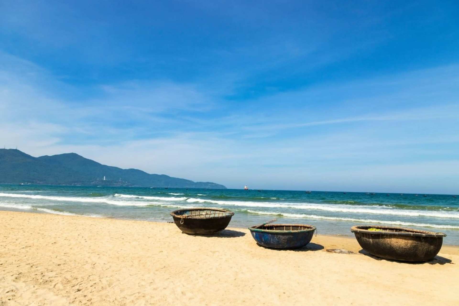 Round basket boats on the sand at Da Nang, the sea and a mountain headland behind