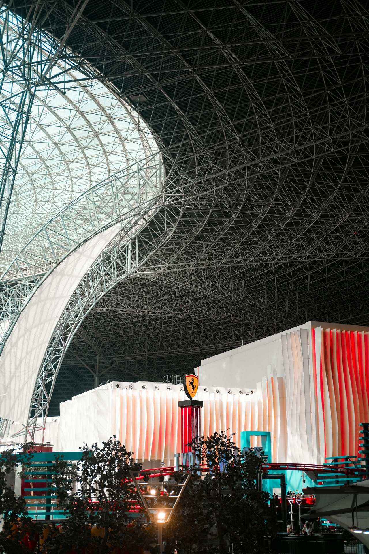 White steel ribs sweeping up under a vast indoor roof, above a red and white pavilion