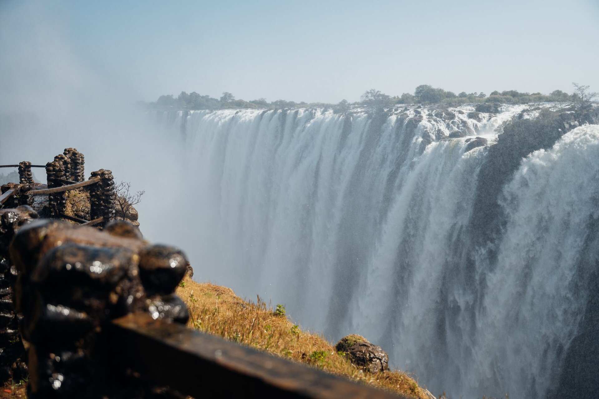 The main curtain of Victoria Falls in full flow, seen from the rim path along the top of the gorge, spray drifting across the falls